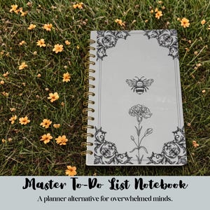 May include: A light gray spiral-bound notebook featuring a black line art illustration of a bee and a flower, framed by ornate corner flourishes. The cover includes the text Master To-Do List Notebook, A planner alternative for overwhelmed minds.