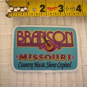 May include: A rectangular patch with the text "BRANSON MISSOURI Country Music Show Capital" in gold and pink lettering. A guitar graphic is in the center. The patch is approximately 3 inches wide.
