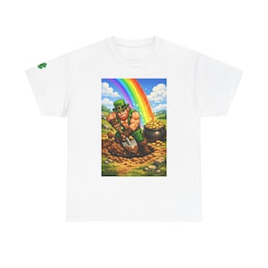 Puede incluir: Camiseta blanca con una colorida ilustración de un duende cavando en busca de oro al final de un arcoíris. El duende lleva un sombrero y un atuendo verdes. Se ve una olla de oro. Un pequeño trébol verde está en la manga izquierda.
