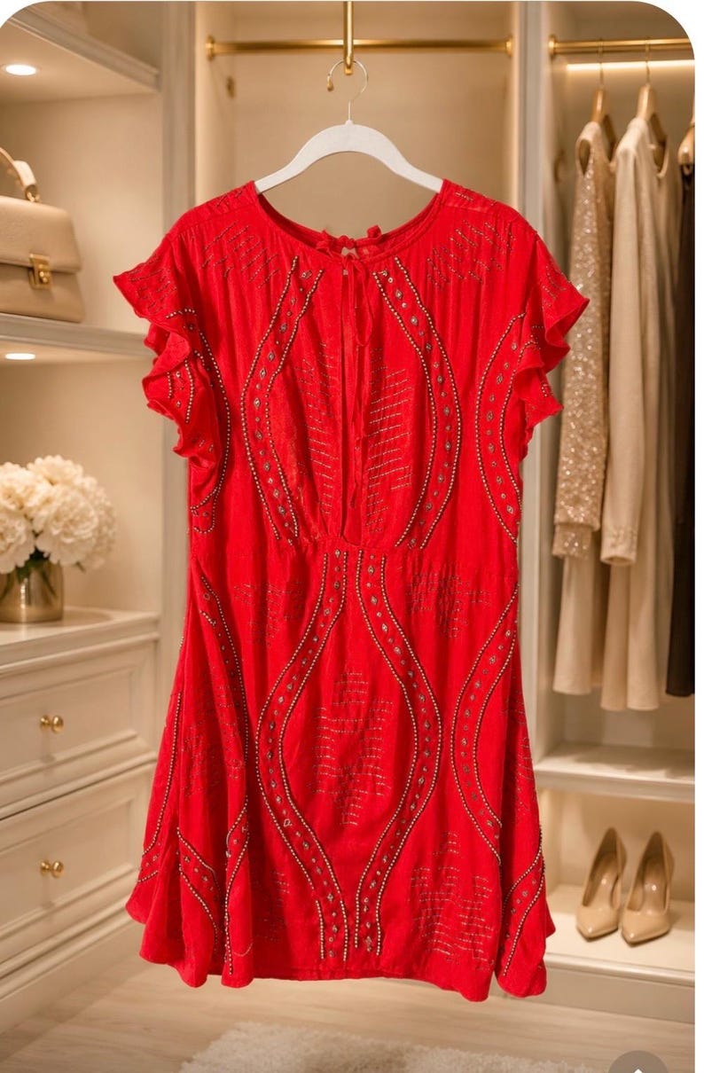 May include: A vibrant red dress with short, ruffled sleeves hangs on a white hanger. The dress features intricate beaded detailing and a flowing silhouette. The dress is displayed in a well-lit closet, suggesting a focus on fashion and apparel.
