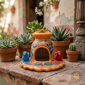 May include: A vibrant, hand-painted ceramic birdhouse in shades of orange, blue, and red. The birdhouse features a decorative design with two small bird figurines and is surrounded by potted succulents and cacti.