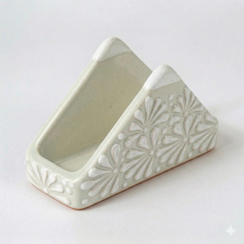 Peut inclure: Un porte-serviettes triangulaire en c&eacute;ramique avec un vernis blanc cass&eacute; brillant. L'ext&eacute;rieur pr&eacute;sente un motif floral blanc en relief avec des motifs en forme de p&eacute;tales couvrant les c&ocirc;t&eacute;s. Les bords sup&eacute;rieurs sont finis en blanc uni.
