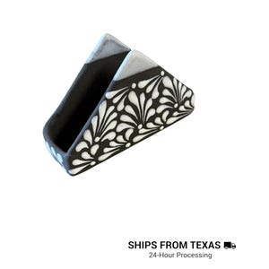 Peut inclure: Un porte-serviettes triangulaire en c&eacute;ramique avec une finition noire mate et un motif floral peint &agrave; la main en blanc. Les bords sup&eacute;rieurs pr&eacute;sentent un &eacute;mail gris clair lisse et l'int&eacute;rieur est fini en noir mat uni. Design ouvert.