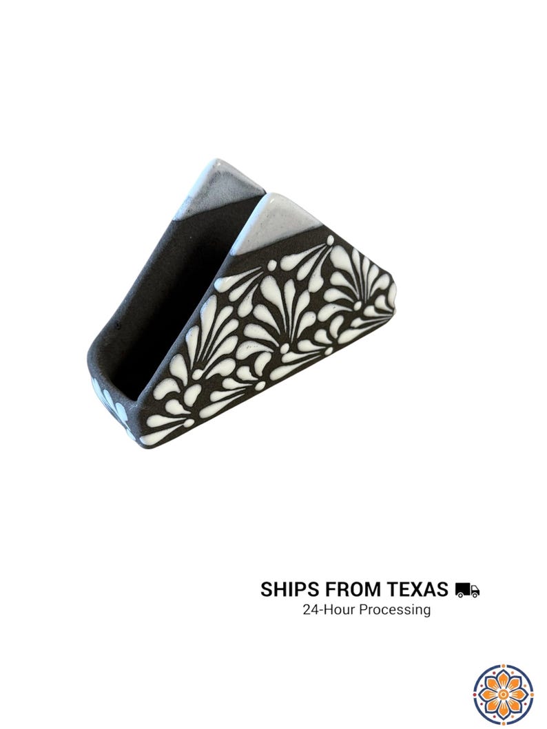 Peut inclure: Un porte-serviettes triangulaire en c&eacute;ramique avec une finition noire mate et un motif floral peint &agrave; la main en blanc. Les bords sup&eacute;rieurs pr&eacute;sentent un &eacute;mail gris clair lisse et l'int&eacute;rieur est fini en noir mat uni. Design ouvert.