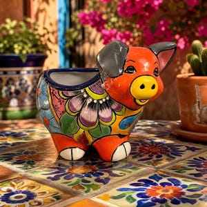 May include: A ceramic pig-shaped planter featuring a vibrant, multi-colored floral pattern painted in shades of orange, blue, purple, and green. The pig has a bright yellow snout, grey ears, and a glossy finish, with a hollow opening at the top.