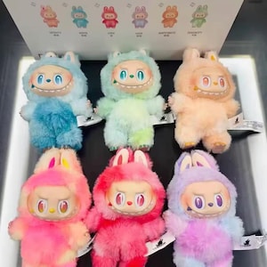 May include: Six colourful plush bunny dolls, each with a distinctive face and hooded outfit. The dolls are in shades of blue, green, pink, and purple. They are displayed with a box featuring small bunny illustrations and the words "Loyalty", "Hope", "Love", "Joy", "Happiness", and "Serenity".