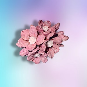 May include: A cluster of sculpted ceramic flowers featuring glossy, textured pink petals with small, white, spiraled centers. The arrangement consists of multiple overlapping blossoms with a shiny, glazed finish, creating a dimensional floral form.