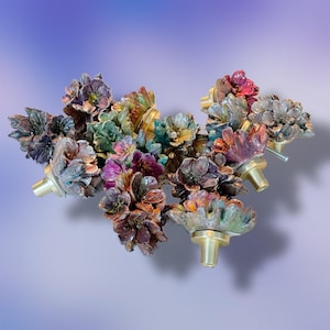 May include: A collection of colorful floral cabinet knobs. The knobs feature intricate flower designs in shades of purple, green, gold, and red. Each knob has a brass base and a stem for mounting.