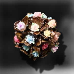 May include: A spherical decorative object featuring a cluster of dark brown, glossy, textured petal-like shapes interspersed with small, molded floral accents in pastel shades of pink, blue, lavender, and cream, creating a dense, multi-layered surface.