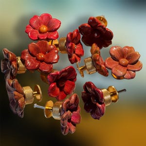 May include: A collection of red flower-shaped cabinet knobs with gold-colored hardware. The knobs are made of a glossy material and feature detailed petal designs. These decorative knobs are ideal for adding a floral accent to furniture.