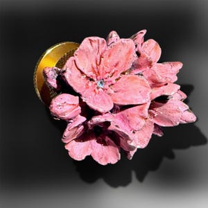 Op de afbeelding: Een decoratieve knop met een cluster van getextureerde, oudroze bloemblaadjes. Het midden van de hoofd-bloem is geaccentueerd met een enkele, kleine, lichtblauwe kristal. De basis van de knop is een rond, goudkleurig metalen hardware-onderdeel.
