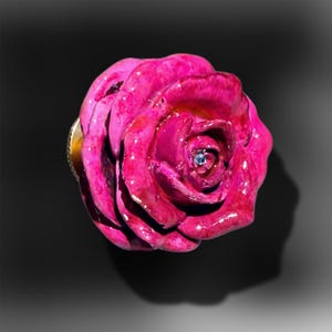 May include: A vibrant fuchsia pink rose-shaped drawer knob with a glossy, reflective finish. The center of the flower features a small, clear, sparkling crystal accent embedded within the petals, attached to a metallic base hardware component.