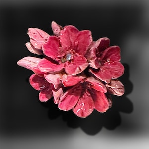 May include: A cluster of deep pink, glossy, sculpted flowers with layered petals and a small, clear, sparkling stone set in the centre of the primary bloom. The floral arrangement features a smooth, reflective finish with subtle variations in colour.