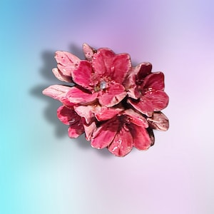 May include: A cluster of deep pink, multi-petaled flowers with a glossy finish. The center of the primary bloom features a small, clear, sparkling crystal accent. The petals exhibit varied shades of magenta and rose, creating a textured appearance.