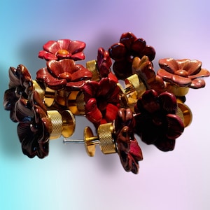 May include: A collection of flower-shaped cabinet knobs in varying shades of red and brown. The knobs have a textured, gold-colored base and a screw for installation. The floral design adds a decorative touch to furniture.