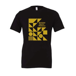 May include: Black t-shirt with a gold geometric design and the text "Jeremy Ayers Pottery" in gold.