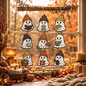 May include: Nine embroidered ghost ornaments hanging from a wooden branch. Each white ghost wears a colorful beanie and holds an autumn-themed item, including a book, candle, bread, donut, mushroom, soup bowl, pumpkin basket, mug, and pinecone.