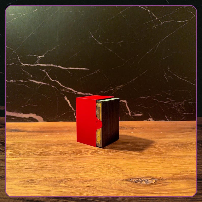 K&ouml;nnte beinhalten: Eine rechteckige Kartenbox mit einer leuchtend roten Au&szlig;enh&uuml;lle und einem dunklen, strukturierten Innenfach, das einen Stapel Spielkarten enth&auml;lt. Die Box verf&uuml;gt &uuml;ber einen halbkreisf&ouml;rmigen Ausschnitt an der Seite f&uuml;r den Zugriff.