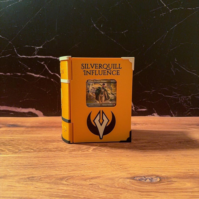 May include: A bright yellow, book-shaped storage case featuring the text Silverquill Influence at the top and a black emblem below. A rectangular cutout in the center displays a trading card depicting a figure in a suit. The case has white corner accents.