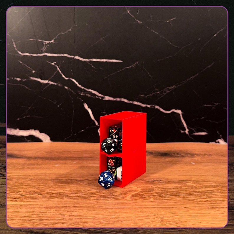 May include: A bright red, rectangular, two-tiered storage tower made of plastic, designed to hold polyhedral dice. The tower features an open front, with several multi-sided gaming dice in black, blue, and white colors resting inside the compartments.