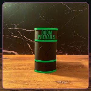May include: A cylindrical black container with bright green trim and horizontal bands. The text DOOM PREVAILS is printed in green on the upper section. A stylized geometric emblem is embossed in the center, with three small icons below it.