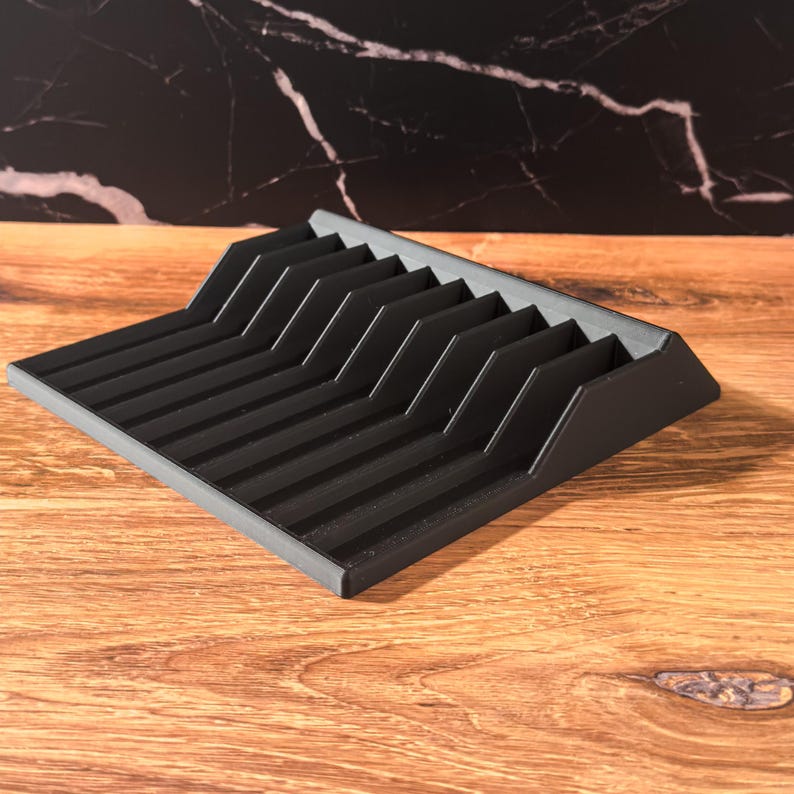 May include: A black knife block with multiple slots for storing knives. The block is made of a dark material and sits on a wooden surface. The design features angled dividers for each knife.