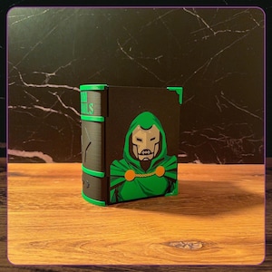 May include: A black rectangular storage box with a green and black graphic of a masked character in a hooded cloak on the front. The side features green accents and the text DOOM NAILS in green lettering. The box has green corner protectors.