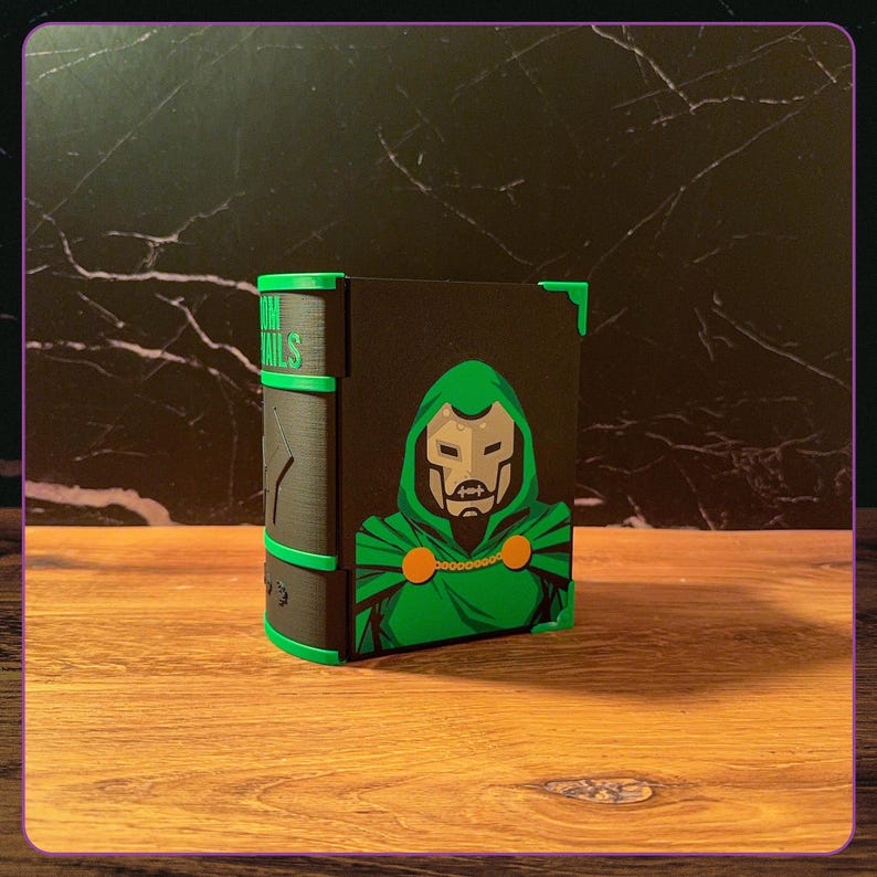May include: A black rectangular storage box with a green and black graphic of a masked character in a hooded cloak on the front. The side features green accents and the text DOOM NAILS in green lettering. The box has green corner protectors.