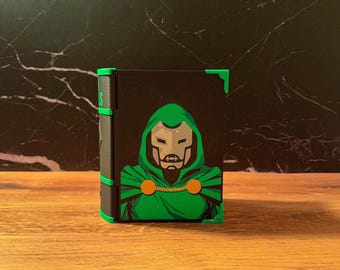 May include: A rectangular black storage box featuring a graphic illustration of a character wearing a green hooded cloak and a metallic mask. The box has bright green corner accents and a black spine with green detailing, presenting a comic book aesthetic.