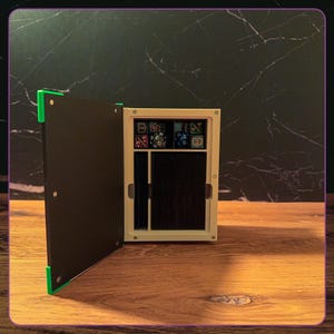 May include: A rectangular storage box with a hinged black door featuring bright green corner accents. The interior is off-white and contains a top compartment filled with various multi-sided gaming dice and a larger lower section holding a deck of cards.