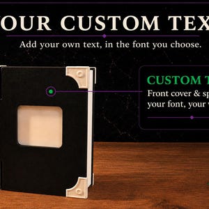 May include: A black book with white corner accents and a central rectangular cutout on the front cover. The text on the image reads YOUR CUSTOM TEXT, Add your own text, in the font you choose, and CUSTOM TEXT Front cover & spine &mdash; your font, your words.