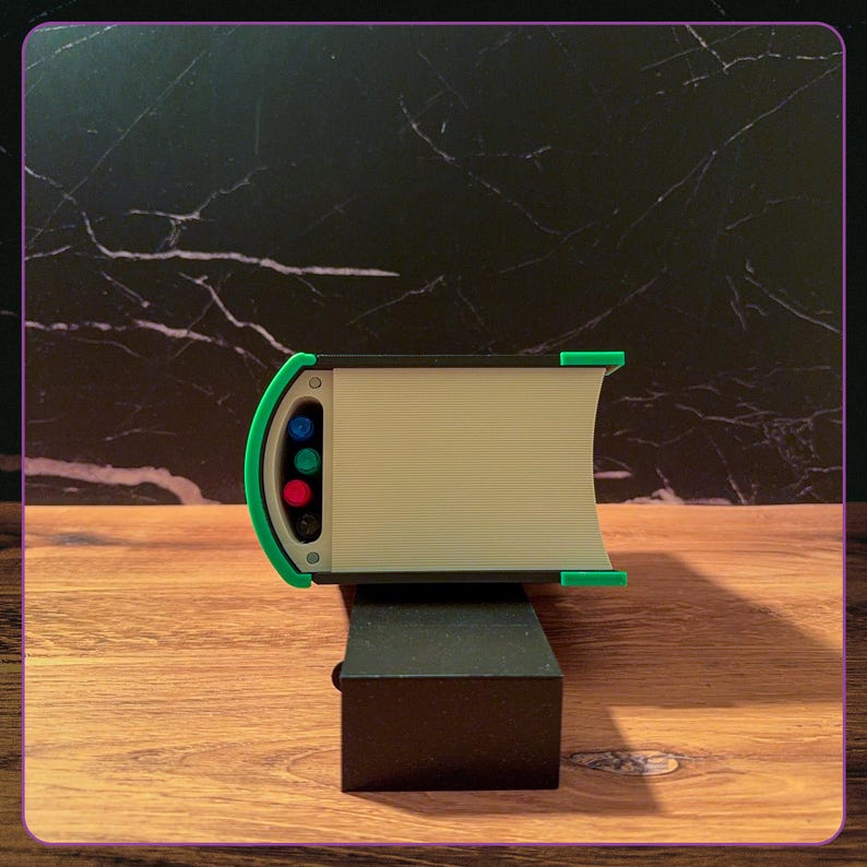 May include: A rectangular object with a cream-colored body and a bright green frame. The side features a vertical panel with four small circular inserts in blue, green, red, and black, set against a dark, textured, marble-like background.