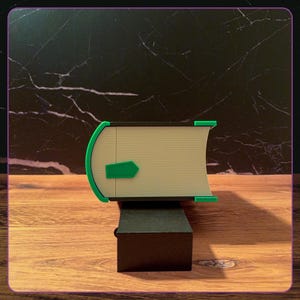 May include: A rectangular object resembling a book with a cream-colored spine and pages, featuring bright green corner accents and a small green arrow-shaped tab on the side. The structure is supported by a solid black rectangular base.