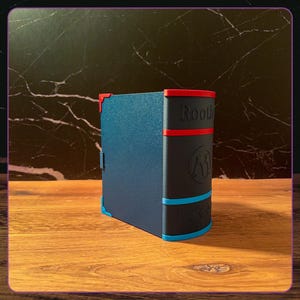 K&ouml;nnte beinhalten: Eine dunkelblaue, buchf&ouml;rmige Aufbewahrungsbox mit schwarzem Buchr&uuml;cken. Der R&uuml;cken ist mit roten und blauen horizontalen Streifen, dem Schriftzug "Rooth", einem kreisf&ouml;rmigen Logo und f&uuml;nf kleinen gepr&auml;gten Symbolen versehen.
