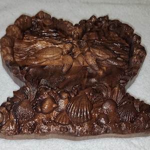 May include: A carved wooden sculpture depicting a marine scene. The sculpture features turtles, seashells, and aquatic plants. The piece is finished in a dark brown stain, highlighting the intricate details of the carving.