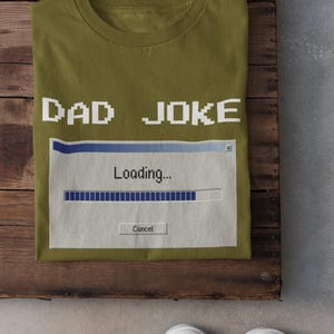 May include: Olive green t-shirt with the text "DAD JOKE" in pixelated white letters. Below, a graphic of a loading bar with the word "Loading..." and a "Cancel" button. White sneakers are visible at the bottom.