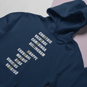 Real Madrid players lineup in their iconic white kits, standing side by side with a strong and determined presence. The backdrop captures the energy of the stadium, highlighting the unity and championship spirit of the team. Perfect for passionate Madridistas and football fans alike.