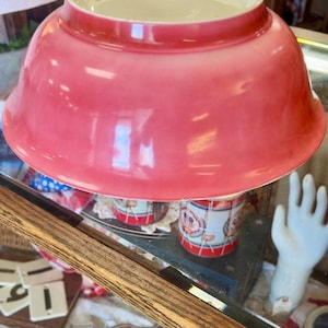 Puede incluir: Un cuenco mezclador redondo invertido con un acabado liso y brillante en un vibrante color rosa coral. El cuenco presenta un borde ancho y acampanado y una base interior blanca, colocado boca abajo para mostrar su superficie exterior uniforme.