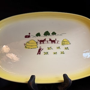 Peut inclure: Un plat de service ovale en céramique avec un centre crème et un large bord jaune. Le centre présente une illustration graphique d'une scène de ferme avec une grange rouge, des arbres verts, deux chevaux marron, des meules de foin jaunes.