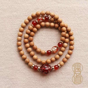 May include: A multi-layered bracelet composed of smooth, light brown wooden beads interspersed with small, polished red stone beads, clear glass beads with gold-colored flakes, and a central, ornate, dark red patterned bead.