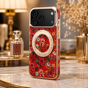 May include: A smartphone case with a vibrant red background featuring a dense floral pattern of pink, yellow, and blue flowers. The case includes a gold-toned metallic frame and a circular gold kickstand ring with the text Premium Kickstand Designed By Denior.