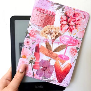 May include: A black Kindle e-reader with a decorative cover featuring a pink cake, flowers, lipstick, and the text "pretty little things." The cover has a glittery, floral design with a heart-shaped strawberry.