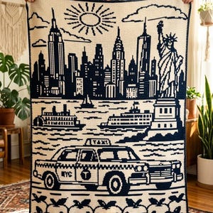 Peut inclure: Une couverture rectangulaire en crochet présentant un motif bleu marine foncé et crème représentant les gratte-ciel de New York, la Statue de la Liberté, un ferry, un taxi avec le texte NYC et T, et une bordure de pommes.