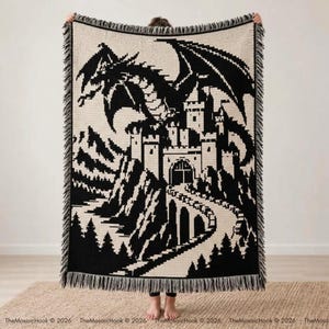 Può includere: Una coperta tessuta rettangolare con un design grafico ad alto contrasto in nero e crema. Il motivo raffigura un grande drago appollaiato sopra un castello di pietra con un sentiero tortuoso che conduce all'ingresso, rifinito con bordi sfrangiati.