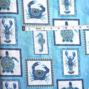 May include: Blue fabric with a repeating pattern of sea creatures including crabs, lobsters, turtles, and seahorses. Each creature is framed in a white rectangle with a decorative border. A measuring tape shows a length of 9 inches.