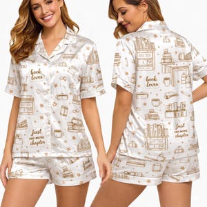 May include: White satin pajama set with a book-themed print. The set includes a short-sleeved button-down shirt and matching shorts. The print features books, coffee cups, and the phrases "book lover" and "just one more chapter."