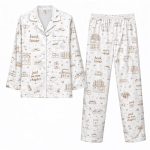 May include: White pajama set with a brown book-themed pattern. The button-down shirt and pants feature illustrations of books, book stacks, and the phrases "book lover" and "just one more chapter."