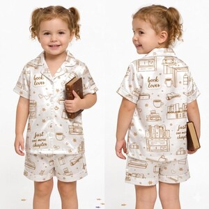 May include: White pajama set with a repeating pattern of books, coffee cups, and bookshelves. The text "book lover" and "just one more chapter" are printed on the front and back of the shirt. The shorts have a matching pattern.