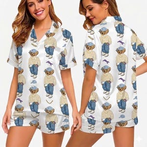 Puede incluir: Conjunto de pijama de sat&eacute;n blanco con un estampado repetido de un oso de peluche con gorra azul, su&eacute;ter y vaqueros. El conjunto incluye una camisa de manga corta con botones y pantalones cortos a juego. El pijama tiene un corte holgado.