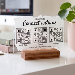 Könnte beinhalten: Ein durchsichtiges Acrylschild mit weiß bemaltem Hintergrund und dem Text Connect with us, Scan Code sowie Scan the code with your phone camera. Es enthält drei QR-Codes mit den Beschriftungen Cash App, Venmo und Instgram auf einem Holzsockel.